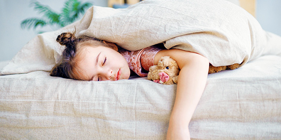 young girl sleeps comfortably in her bed with small teddy bear